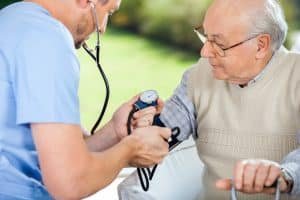 Male CNA checking blood pressure of senior man at nursing home